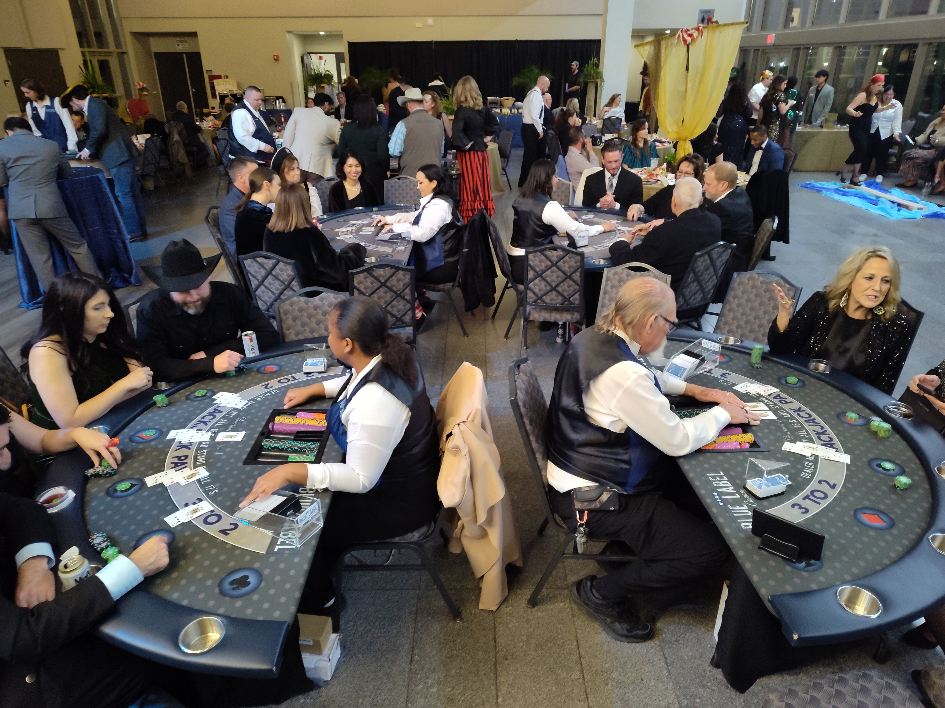 Wide-angle overhead view of multiple Blue Label blackjack tables with dealers and guests at a Houston casino party