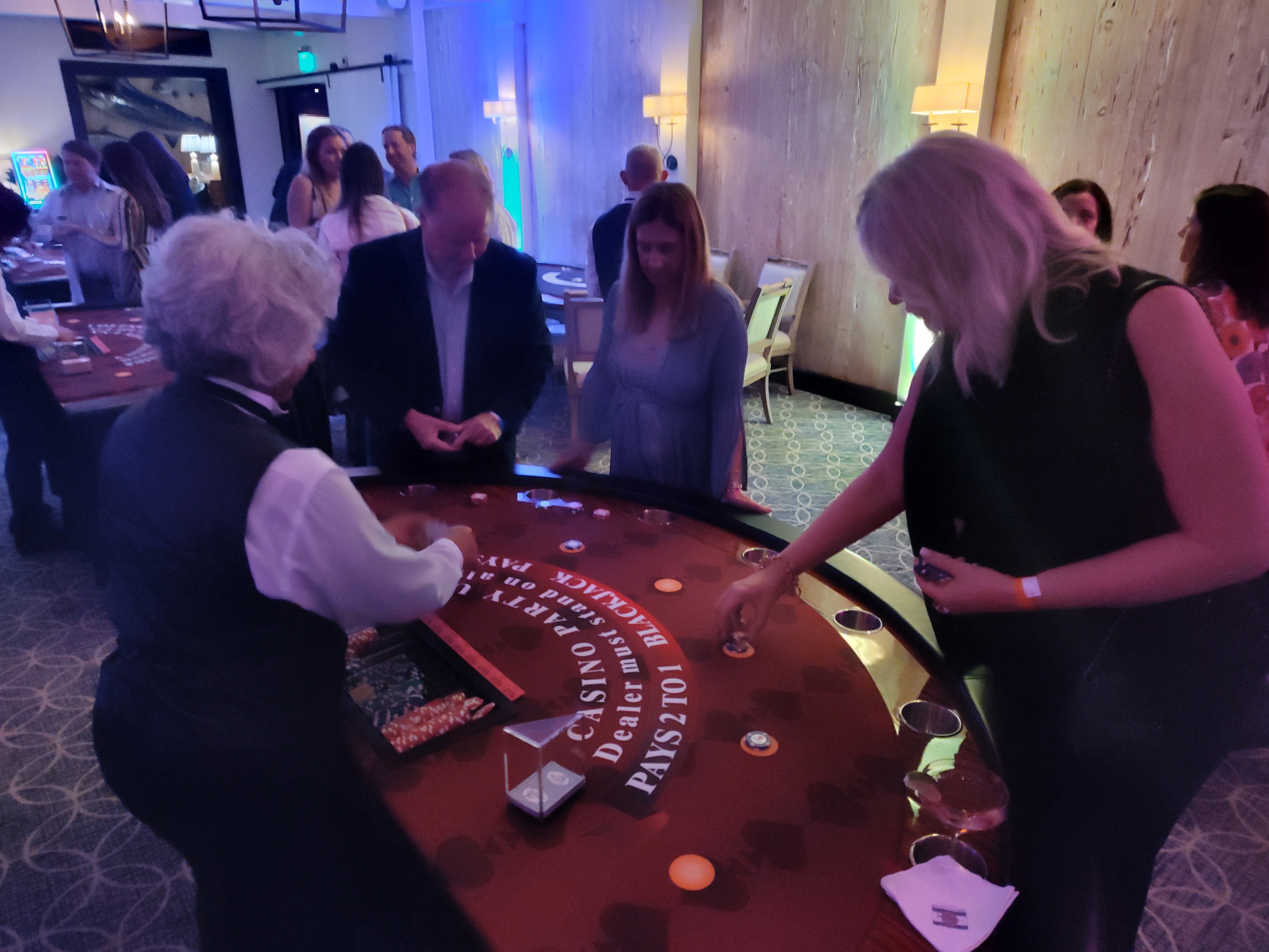 Guests playing blackjack at a Casino Party USA table with blue uplighting in Miami