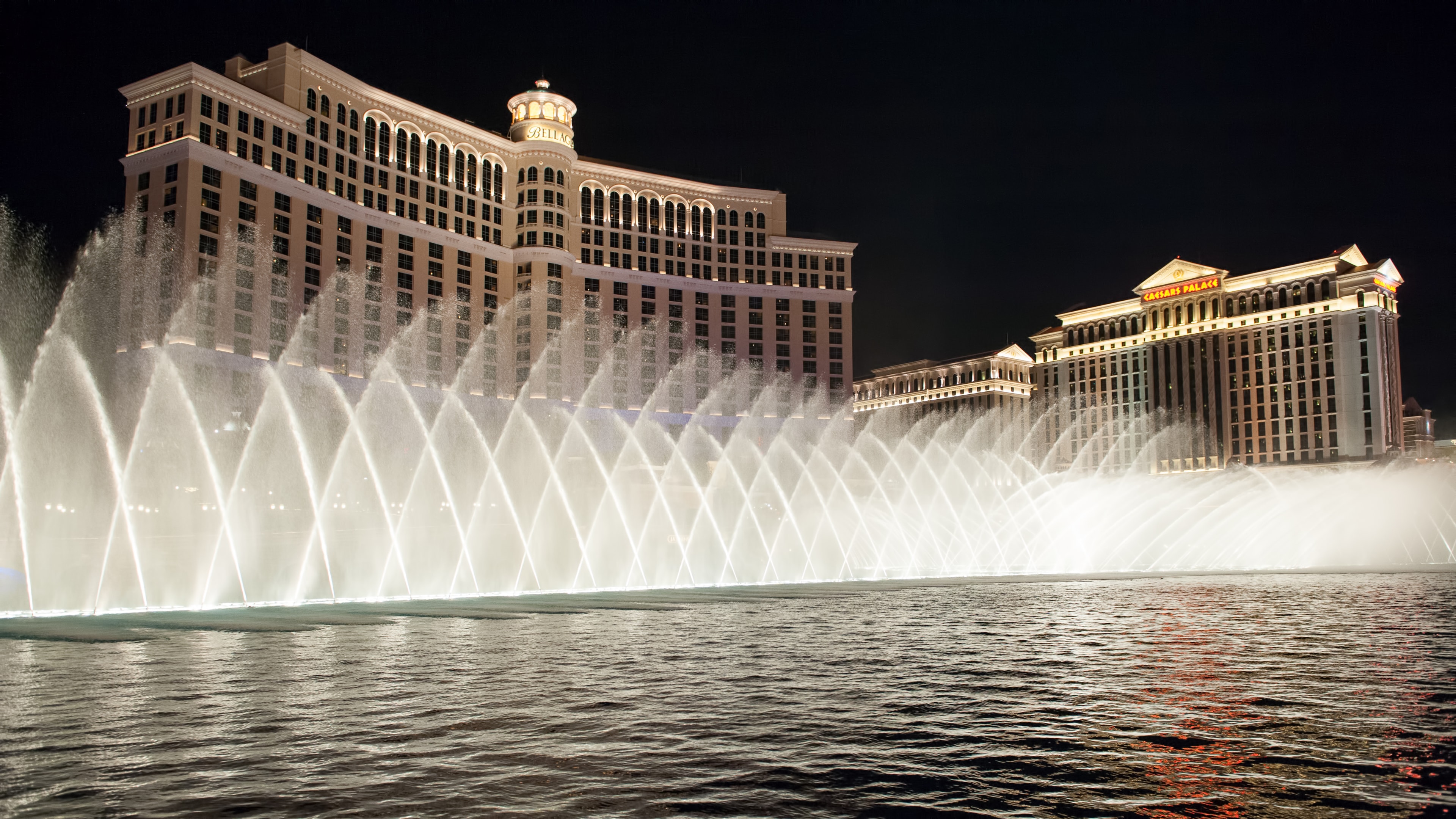 Bellagio fountains illuminated at night with Caesars Palace in the background on the Las Vegas Strip